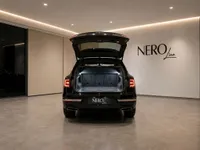 The rear view of a black Bentley Bentayga V8 with its trunk open, parked in a luxury showroom in Zurich.