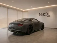 The 2022 Bentley Continental GT in Satin Anthracite Grey is parked at a showroom in Lausanne, showcasing its elegant rear three-quarter view.