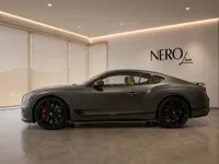The 2022 Bentley Continental GT in Satin Anthracite Grey, showcasing its elegant side profile indoors at a showroom in Lausanne.