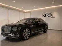 The black 2023 Bentley Flying Spur luxury sedan is displayed at a front three-quarter angle in a modern showroom in Lausanne.