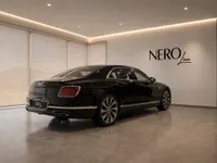 The black Bentley Flying Spur 2023 is parked in a showroom with the NERO line logo on the wall, Lausanne.