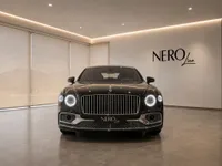 The glossy black 2023 Bentley Flying Spur luxury sedan is prominently displayed in a showroom in Lausanne, front view.