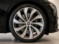 The elegant front wheel with silver and black multi-spoke rim and gloss black body of the Bentley Flying Spur in Lausanne.