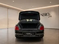 Rear view of a black Bentley Flying Spur with its trunk open, parked in a modern showroom in Lausanne.