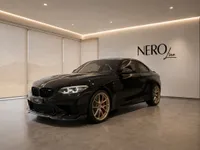A glossy black BMW M2 CS is parked at a front three-quarter angle in a modern showroom in Zurich.