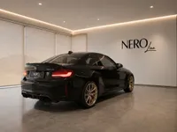 The gloss black BMW M2 CS with gold wheels is parked in a modern showroom in Zurich, viewed from the rear three-quarter angle.