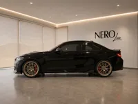 The black 2020 BMW M2 CS is showcased in a showroom in Zurich, featuring its sleek side profile, gold wheels, and red brake calipers.