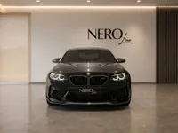 A sleek gloss black BMW M2 CS is presented from a direct front view in a modern, well-lit showroom in Zurich.