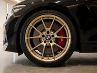 The front wheel of a black BMW M2 CS in Zurich, featuring a gold multi-spoke rim and a prominent red brake caliper.