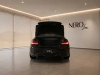 The black BMW M2 CS is shown from the rear with its trunk open, parked in a modern showroom in Zurich.