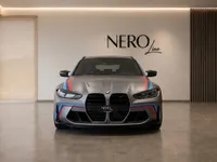 Front view of the matte grey BMW M3 Competition Touring with M-stripes, parked in a modern showroom in Zurich.