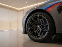 The BMW M3 Competition Touring in matte grey showcases its front wheel with blue brake calipers and M stripes in Zurich.