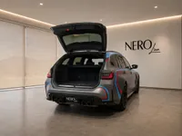 The matte grey BMW M3 Competition Touring with its trunk open, showcasing the spacious cargo area in a Zurich showroom.