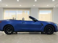 El BMW M4 Competition Cabrio azul Frozen Portimao mate se ve de lado con la capota bajada, aparcado en el interior en Ibiza.