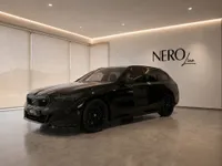 The black 2025 BMW M5 Touring, shown from a front three-quarter angle, is parked in a modern NEROline showroom in Zurich.