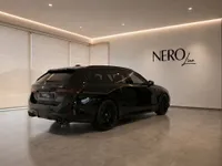 The Gloss Black 2025 BMW M5 Touring is showcased from a rear three-quarter angle inside a modern showroom in Zurich.