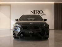 The sleek black 2025 BMW M5 Touring is showcased from a direct front view in a modern showroom in Zurich.