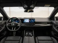 The luxurious cockpit of the 2025 BMW M5 Touring in Zurich, featuring a modern dashboard with dual digital displays and a sporty steering wheel.