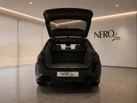 The rear view of the black 2025 BMW M5 Touring with its trunk open, parked in a showroom in Zurich.