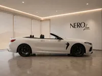 A sleek white 2021 BMW M8 Competition Cabriolet is showcased from its side profile with the top down in a modern Lausanne showroom.