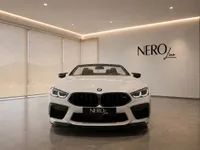 The white 2021 BMW M8 Competition Cabriolet is shown from the front, parked in a modern showroom in Lausanne with the NEROline logo.