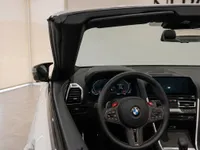 The luxurious interior of the BMW M8 Competition Cabriolet in Lausanne, showing the steering wheel and dashboard with the convertible top down.