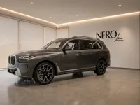 The metallic dark grey 2023 BMW X7 is parked in a modern showroom in Lausanne, seen from a front three-quarter angle.