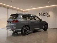 The metallic dark grey 2023 BMW X7 is showcased from a rear three-quarter angle in a modern showroom in Lausanne.