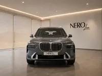The metallic dark grey 2023 BMW X7 is shown from the front, parked indoors in a modern Lausanne showroom.