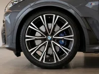 The BMW X7 in metallic dark grey displays its front wheel, with a black and silver multi-spoke rim and a blue M Sport brake caliper, in Lausanne.