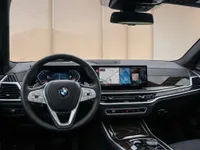 The luxurious interior of the BMW X7 in Lausanne, featuring the steering wheel, digital dashboard, and infotainment screen with elegant wood trim.