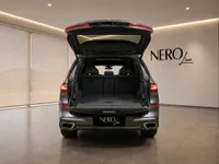 The rear view of a metallic dark grey BMW X7 in Lausanne, showcasing its spacious open trunk and rear design.