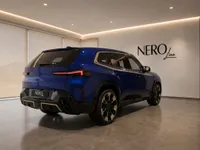 The gloss Deep Blue 2023 BMW XM is showcased from a rear three-quarter angle in a modern showroom in Lausanne.