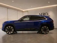 The gloss Deep Blue 2023 BMW XM luxury SUV is parked in a modern showroom in Lausanne, showcasing its sleek side profile.