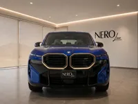 The gloss Deep Blue 2023 BMW XM is showcased from a direct front view inside a modern showroom in Lausanne.