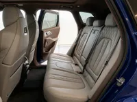The luxurious rear interior of the BMW XM in Lausanne, featuring light-colored leather seats and an open door revealing the gloss Deep Blue exterior.