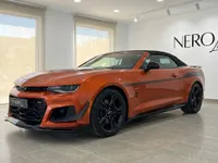 Un Chevrolet Camaro Cabriolet naranja metálico brillante, un deportivo descapotable, se exhibe en un concesionario en Alicante, España, desde una vista frontal tres cuartos.