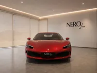 The gloss Rosso Imola metallic red Ferrari 296 GTB is prominently displayed from the front in a showroom in Lausanne.