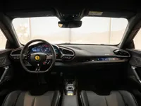 The luxurious black interior and modern digital dashboard of the Ferrari 296 GTB in Lausanne, featuring red stitching and a sporty steering wheel.