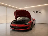 A gloss Rosso Imola metallic red Ferrari 296 GTB is parked indoors in Lausanne, showcasing its open front hood.