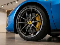 The blue Ferrari 296 GTS showcases its front wheel with a grey multi-spoke rim and distinctive yellow brake caliper in Lausanne.