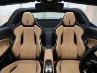 The luxurious interior of the Ferrari 296 GTS in Lausanne, featuring tan leather sports seats with carbon fiber accents and a view of the cockpit.
