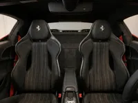 Ferrari 296 GTS interior showcasing black racing seats with white stitching, red seatbelts, and central console in Zurich.