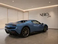 A sleek blue Ferrari 296 GTS is parked indoors, showcasing its elegant rear three-quarter design in a modern showroom.