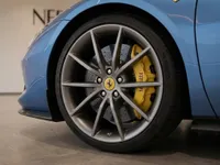 Close-up of the blue Ferrari 296 GTS's front wheel, showcasing the grey multi-spoke rim and yellow brake caliper in Zurich.