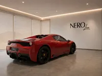 A glossy red Ferrari 458 Spider is parked indoors, shown from a rear three-quarter angle, with the NEROline logo on the wall and mountains visible through blinds in Zurich.