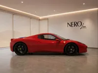 A glossy red Ferrari 458 Spider is showcased in a modern studio, viewed from its elegant side profile in Zurich.