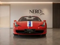 A striking red Ferrari 458 Spider, featuring a distinctive blue and white racing stripe, is parked front-on in a modern showroom in Zurich.
