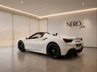 A white Ferrari 488 Spider, with its convertible top down, is parked in a modern showroom in Zurich, showcasing its sleek rear three-quarter view.