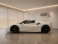 The white Ferrari 488 Spider is showcased in a side profile view with its convertible top down, parked in a modern showroom in Zurich.